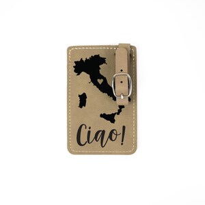 May include: Tan leather luggage tag with a black outline of Italy and a small heart in the center. The text "Ciao!" is printed in black below the map.