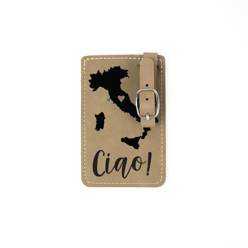 May include: Tan leather luggage tag with a black outline of Italy and a small heart in the center. The text "Ciao!" is printed in black below the map.