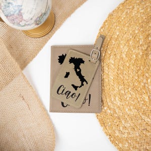 May include: A tan leather passport holder and luggage tag set with a black outline of Italy and the text "Ciao!" on the tag.