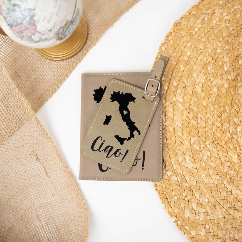 May include: A tan leather passport holder and luggage tag set with a black outline of Italy and the text "Ciao!" on the tag.