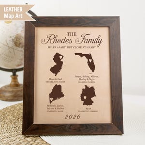 May include: A framed family map art piece with a dark brown wooden frame. The artwork features four state outlines with heart icons, personalized with names and locations. Text includes "The Rhodes Family" and "Miles apart, but close at heart."