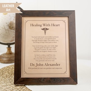 May include: A framed leather art piece with the text "Healing With Heart" and a poem. The frame is dark brown, and the text is in a classic serif font. The artwork includes the name "Dr. John Alexander".