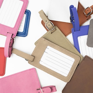 May include: Assortment of colorful leather luggage tags with a stitched border. Each tag has a blank white label with lines for writing name, address, and phone number. The tags have a loop for attaching to luggage.