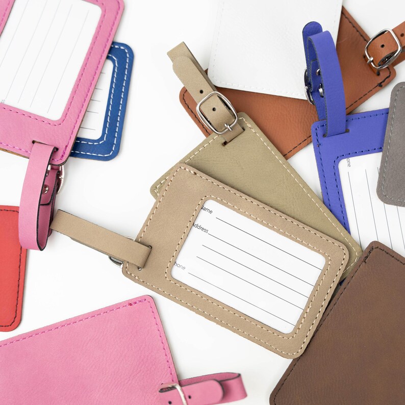 May include: Assortment of colorful leather luggage tags with a stitched border. Each tag has a blank white label with lines for writing name, address, and phone number. The tags have a loop for attaching to luggage.