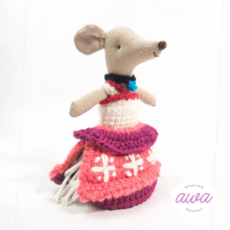 May include: A crocheted doll mouse wearing a pink, white, and red dress with a blue bell necklace. The doll is standing on a white background. The text "weaving awa dreams" is in the lower right corner of the image.
