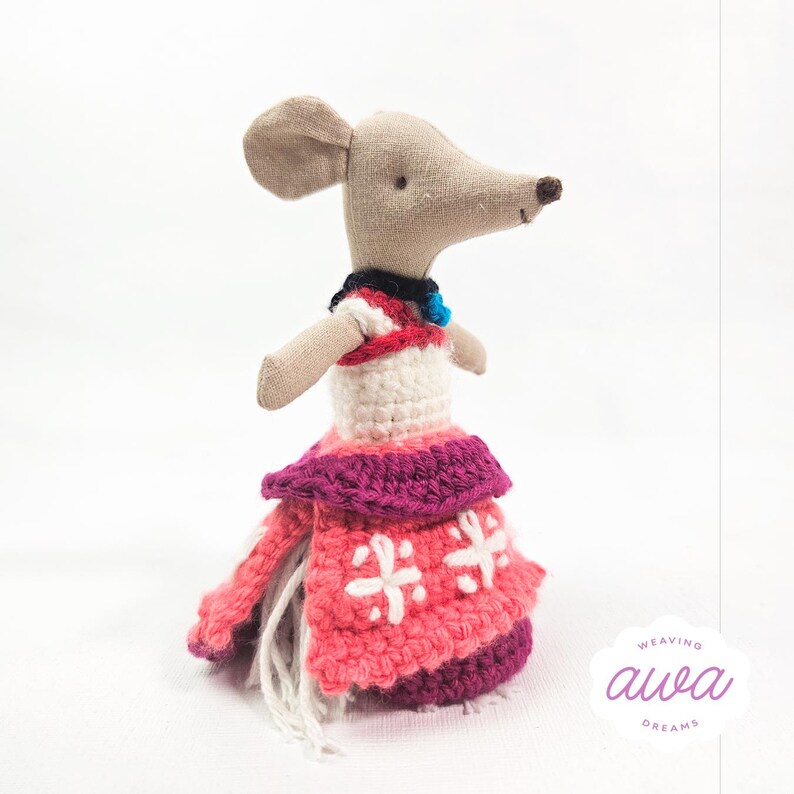 May include: A small crocheted mouse doll wearing a pink and purple dress with white embroidery. The doll has a light brown body and a black collar with a blue bead.