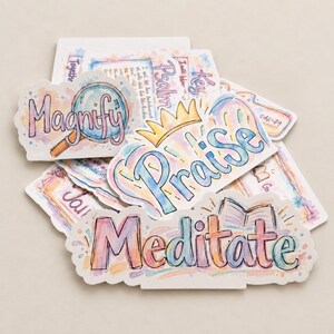 May include: A collection of die-cut stickers featuring watercolor-style lettering and illustrations. The stickers display words including Magnify, Praise, and Meditate, accompanied by icons like a magnifying glass, a crown, and an open book.