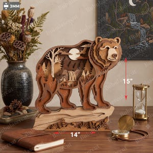 May include: A multi-layered wooden bear sculpture featuring a forest landscape with a waterfall, trees, and a moon cutout. The piece measures 15 inches in height and 14 inches in width, with a material thickness of 3mm, showcasing intricate laser-cut details.
