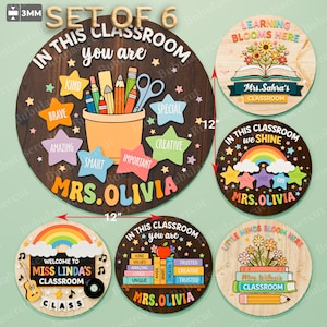 Könnte beinhalten: Set aus sechs Holzschildern für das Klassenzimmer. Die runden Schilder zeigen verschiedene Designs, darunter ein Stifthalter, ein Regenbogen und Bücher. Jedes Schild hat einen Durchmesser von etwa 30 cm, ideal für die Klassenzimmerdekoration.