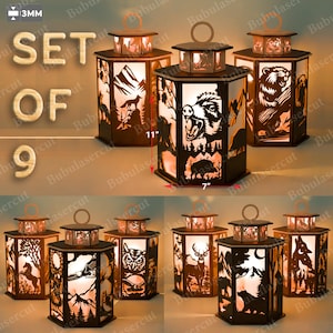 Może przedstawiać: Zestaw dziewięciu dekoracyjnych lampionów z wyciętymi laserowo scenami dzikiej przyrody, w tym niedźwiedź, jeleń i sowa. Każdy lampion ma około 18 cm szerokości i 28 cm wysokości. Lampiony mają ciepły, zachęcający blask.