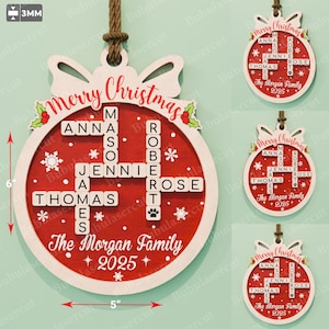 Może przedstawiać: Drewniana ozdoba świąteczna, o wysokości około 15 cm i szerokości 13 cm, z czerwonym środkiem i białym obramowaniem. Ozdoba zawiera krzyżówkę z nazwiskami członków rodziny oraz tekst "Merry Christmas" i "The Morgan Family 2025".