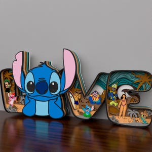 May include: A wooden cutout of the word 'LOVE' with a blue Stitch character from Lilo & Stitch in the first letter. The letters are layered and have a beach scene with palm trees, waves, and other characters from the movie.