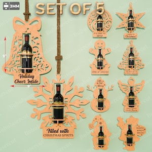 Op de afbeelding: Set van 5 houten wijnfleshouders in diverse kerstvormen, waaronder een bel, sneeuwvlok, ster, peperkoekmannetje, kerstboom, engel, sneeuwpop en kabouter. Elke houder is ontworpen voor een wijnfles. De tekst "Holiday Cheer Inside" is zichtbaar.