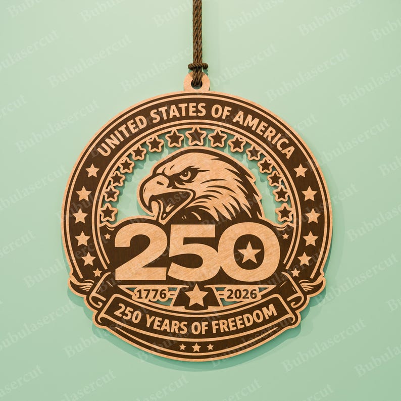 K&ouml;nnte beinhalten: Runder Holzschmuck mit der Aufschrift "UNITED STATES OF AMERICA" und "250 YEARS OF FREEDOM". Zeigt einen Adler, Sterne und die Jahre 1776-2026. Enth&auml;lt eine braune Schnur zum Aufh&auml;ngen. Eine patriotische Dekoration.