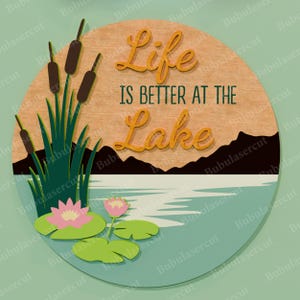 May include: A round wooden sign with the text "Life is Better at the Lake". The sign features a lake scene with cattails, water lilies, and mountains. The text is in a script font.