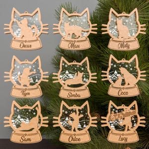 Puede incluir: Nueve adornos de madera para el árbol de Navidad con forma de gato y nombres personalizados. Cada adorno presenta una silueta de gato dentro de un diseño de bola de nieve con una escena de invierno. Los adornos son perfectos para un árbol de Navidad o como regalo para los amantes de los gatos.