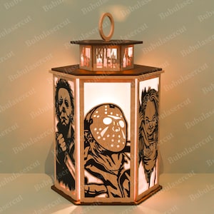 May include: A wooden lantern featuring horror movie characters. The lantern has a hexagonal base with panels depicting Michael Myers, Jason Voorhees, and Chucky. The top section spells out "KILLER" and has a wooden handle.