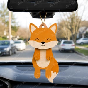 May include: A wooden fox-shaped car charm. The charm is orange with a light brown belly and tail tip. It has a smiling face with closed eyes and is hanging from a string. The charm is designed to hang from a car's rearview mirror.