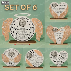 Könnte beinhalten: Set aus 6 Gedenktafeln. Jede Tafel zeigt ein Foto von Matthew (1960-2025) und enthält Sätze wie „Deep in our Hearts“ und „Forever in our Hearts“. Die Holztafeln haben Engelsflügel-Designs. Die größte Tafel ist 33 cm breit.