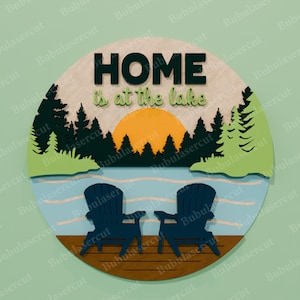 May include: A round wooden sign with a lake scene. The sign features two blue Adirondack chairs on a dock, a lake, trees, and a sunset. The words "HOME is at the lake" are displayed.