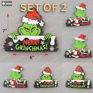 May include: Set of two Grinch-themed Christmas decorations. The Grinch is holding a sign that says "Merry Grinchmas!" and is 15 cm wide and 18 cm tall. The Grinch is wearing a Santa hat and has a green face.