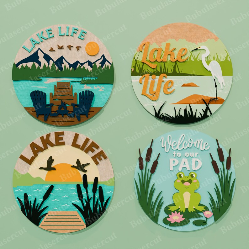May include: Four round wooden lake-themed signs. One sign has the text "LAKE LIFE" with a mountain scene, a dock, and chairs. Another has a heron and the text "Lake Life". The third has the text "LAKE LIFE" with ducks. The fourth has a frog and the text "Welcome to our PAD".