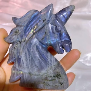 May include: A carved labradorite unicorn head sculpture with iridescent blue and grey colours. The sculpture is detailed with a horn and mane.