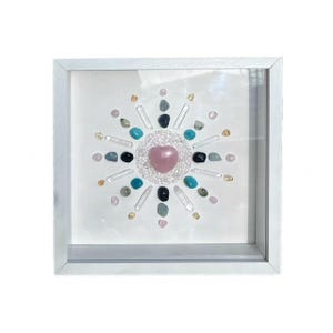 May include: A square art piece in a white frame featuring a crystal mandala design. The mandala has a pink heart-shaped crystal at its centre, surrounded by clear, black, blue and green crystals.