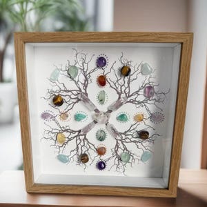 Op de afbeelding: Een ingelijst kunstwerk met een boomachtig ontwerp, versierd met kleurrijke edelstenen. De edelstenen, waaronder amethist en tijgeroog, zijn rond de takken en het midden gerangschikt. Het frame is gemaakt van lichtgekleurd hout.