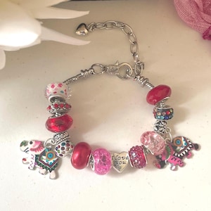 May include: A silver charm bracelet with various beads and charms. The bracelet features red, pink, and clear beads, along with elephant and heart charms. The heart charm has the words "I love you" engraved on it.