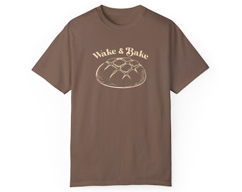 May include: A brown t-shirt with the text "Wake & Bake" in a cream colour and a drawing of a round loaf of bread in the same cream colour.
