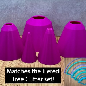 May include: Five magenta cone-shaped objects of different sizes, with a set of blue and teal arched cutters. The text "Matches the Tiered Tree Cutter set!" is displayed in a black rectangle. The objects are arranged on a wooden surface. Ideal for baking.
