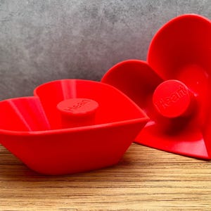 May include: Two red heart-shaped silicone molds with the word "Heart" embossed on the front.