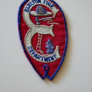 May include: A red and blue embroidered patch with the text "Carlton Fire Department" in white. The patch features a firefighter with a ladder and a fire hydrant.