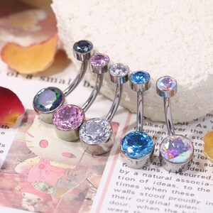 May include: A collection of curved belly button rings with colorful, iridescent gemstones. The jewelry features a silver-tone metal and a variety of jewel tones, including blue, purple, and clear stones. The gems are round and set in a simple, elegant design.