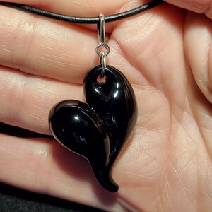 A black heart-shaped pendant necklace with a sterling silver bail. The pendant is made of smooth, shiny black glass and has a unique, asymmetrical shape.