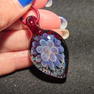 Detailed view of a lampworked glass pendant with a pale lavender implosion pattern layered over a rich red background with shimmering blue accents, emphasizing its three-dimensional depth.