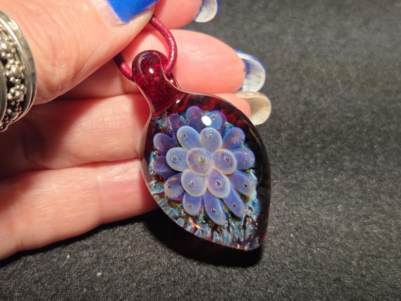 Detailed view of a lampworked glass pendant with a pale lavender implosion pattern layered over a rich red background with shimmering blue accents, emphasizing its three-dimensional depth.