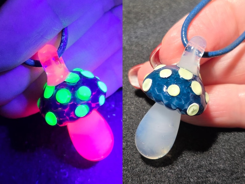 Split image of the same handmade borosilicate glass mushroom pendant shown in regular light and under UV reactive black light. In normal light, the mushroom has a blue frit cap with pale yellow raised dots and a soft milky white stem. Under black light, the pendant dramatically color shifts with neon green glowing dots, a bright pink glowing stem, and a pink-purple cap, highlighting the UV reactive glass details.
