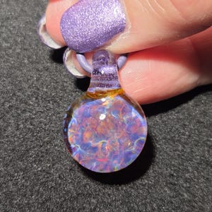 Small hand blown borosilicate implosion pendant with layered purple, blue, pink and golden frit, photographed against a dark background.