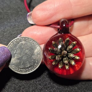 Pendant size compared to a quarter and it is larger measuring 1.4 inches long with the glass bail.  The round portion measures 1 inch diameter.