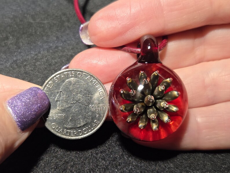 Pendant size compared to a quarter and it is larger measuring 1.4 inches long with the glass bail.  The round portion measures 1 inch diameter.