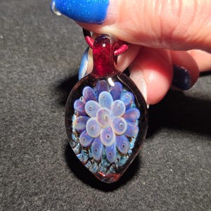 Close-up of a handcrafted glass implosion pendant with soft lavender petals layered over a rich red and blue-sparkle background, highlighting the dimensional depth and polished glass surface.