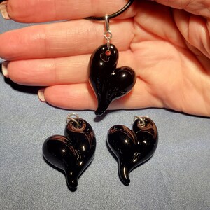 Three black glass heart shaped pendants with sterling silver bails. The pendants are on a blue surface.