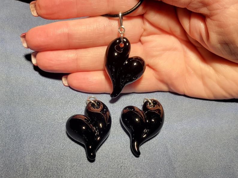 Three black glass heart shaped pendants with sterling silver bails. The pendants are on a blue surface.