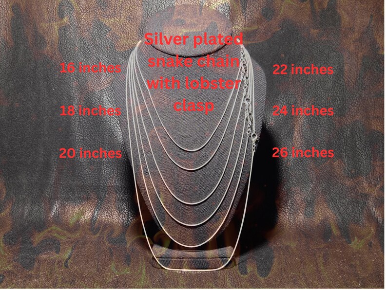 Display bust showing multiple silver-plated snake chains layered by length, labeled from 16 to 26 inches, each with a lobster clasp, demonstrating available necklace length options on a dark textured background.