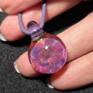 Small boro implosion choker pendant with a colorful flower-like frit design in pink, violet and blue that shifts in appearance with different backgrounds.