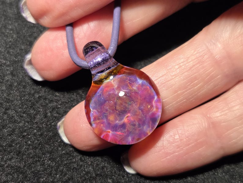 Small boro implosion choker pendant with a colorful flower-like frit design in pink, violet and blue that shifts in appearance with different backgrounds.