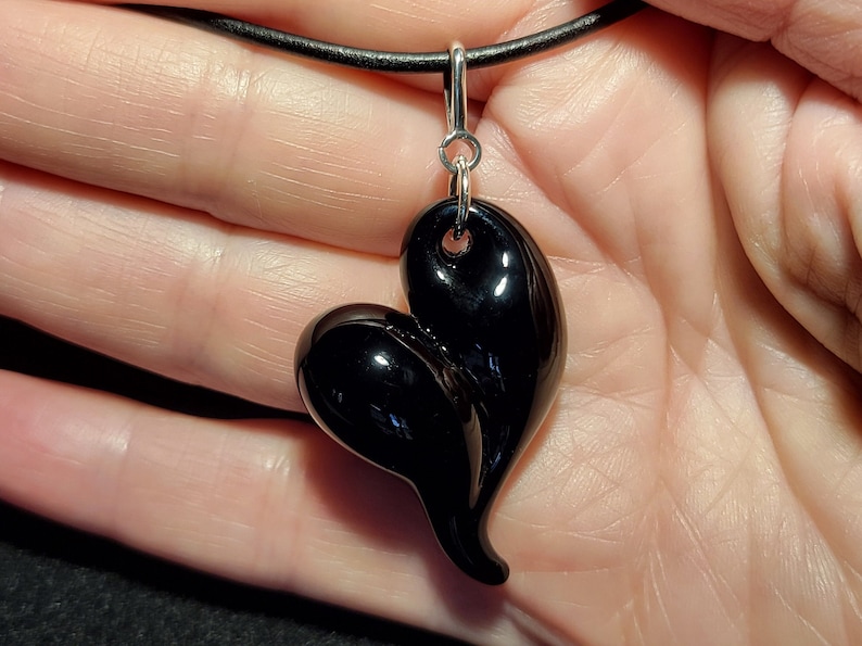 A black heart-shaped pendant necklace with a sterling silver bail. The pendant is made of smooth, shiny black glass and has a unique, asymmetrical shape.