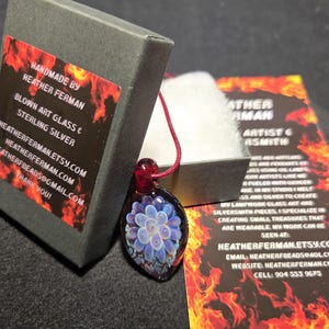 Image of the pendant and a jewelry box labeled with the business name. A business bookmark explains the glassmaking process, accompanying the pendant for a complete gift presentation.